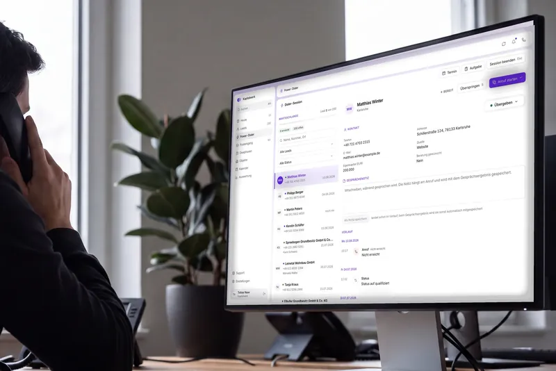 Closer mit dem Hörer am Ohr am Schreibtisch, von hinten aufgenommen, auf dem Bildschirm der Power-Dialer mit Warteschlange, Kontaktdaten und Gesprächsverlauf